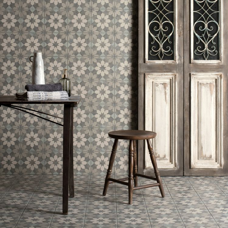 Decorative tiles with floral pattern on a wall and floor, wooden stool and table in the foreground.