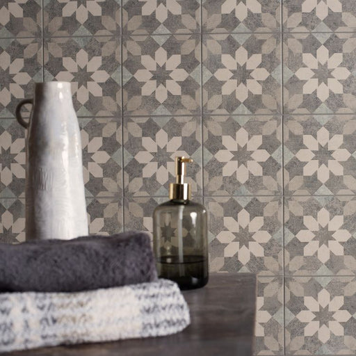 Bathroom setting with patterned tiles, towels, and bottles on a wooden surface.