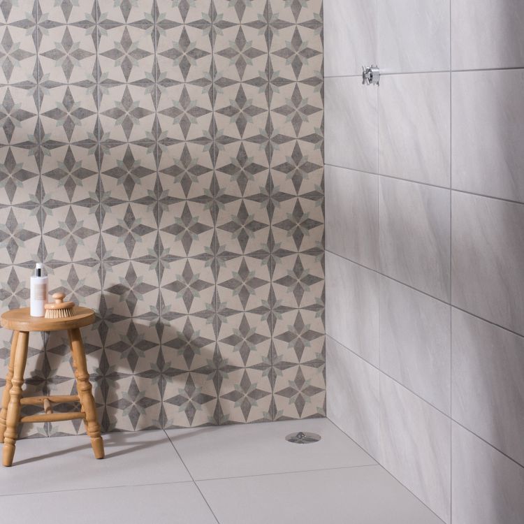 Image of Bathroom space with patterned star‑design wall tiles, light grey rectangular wall tiles, and a small wooden stool holding toiletries.”