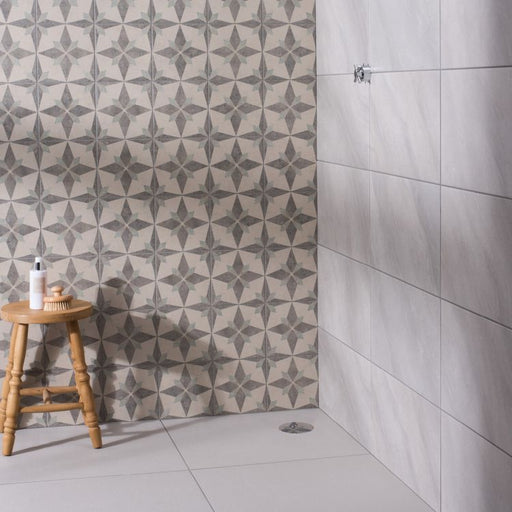 Bathroom space with patterned star‑design wall tiles, light grey rectangular wall tiles, and a small wooden stool holding toiletries.”