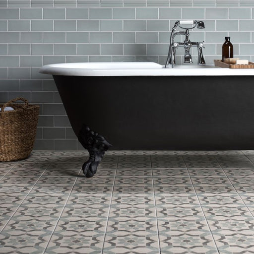 Bathroom with a freestanding black clawfoot bathtub, grey subway‑tile wall, and patterned floor tiles, with a woven basket placed to the side
