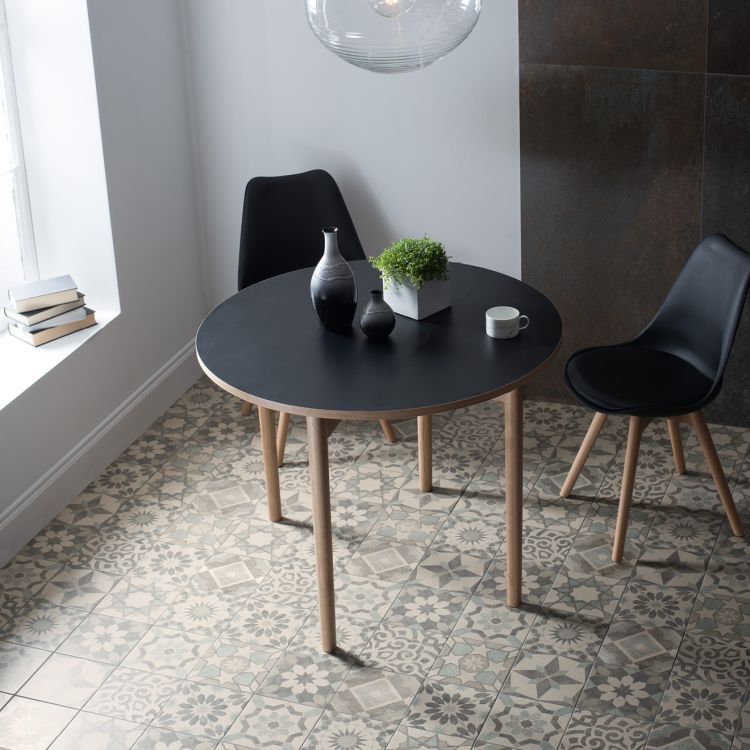 Image of Round black table with two black chairs in a room with patterned tiles.