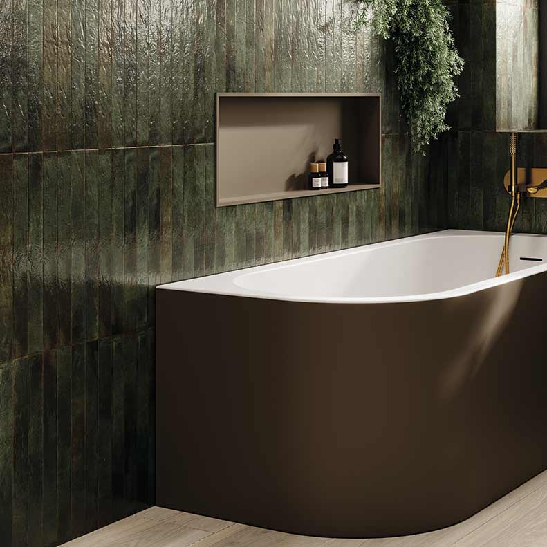 A modern freestanding bathtub in a dark brown finish with a white interior, set against a textured dark green tiled wall with a recessed shelf holding small toiletries.