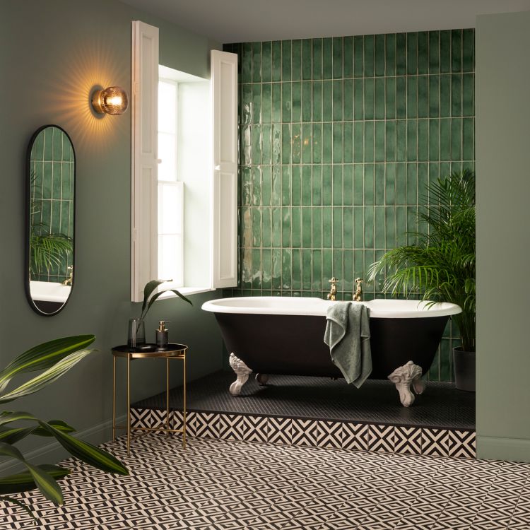Image of Bathroom with a black clawfoot bathtub on a raised platform, green vertical wall tiles, geometric black‑and‑white floor tiles, and several potted plants