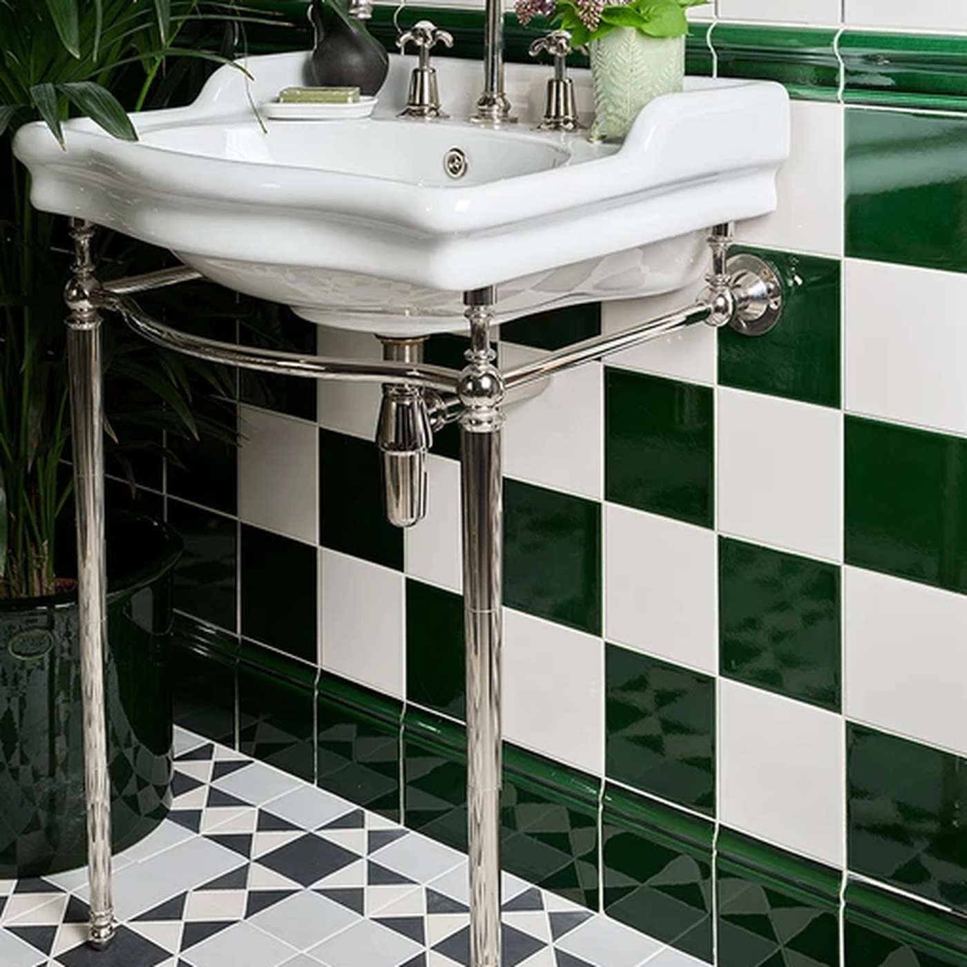 Image of Bathroom with a white sink on a metal stand against a green and white tiled wall.