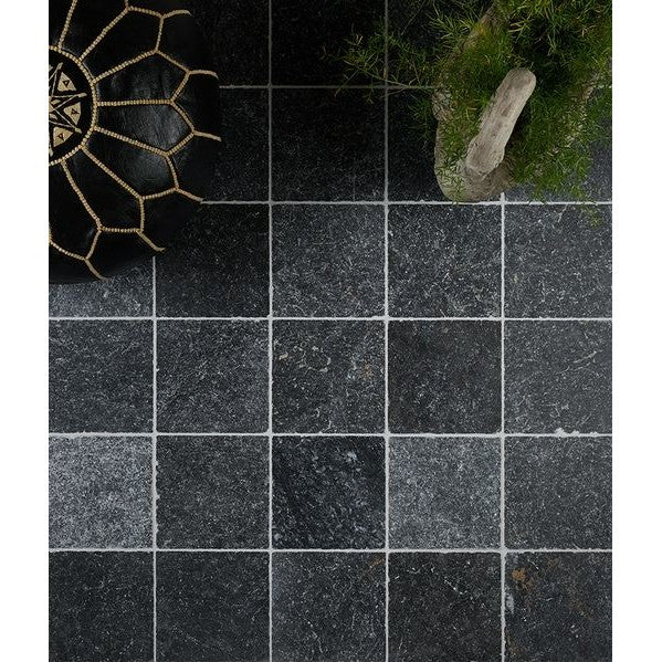 Image of Black square tiles on a dark surface with a decorative object and greenery in the corner.