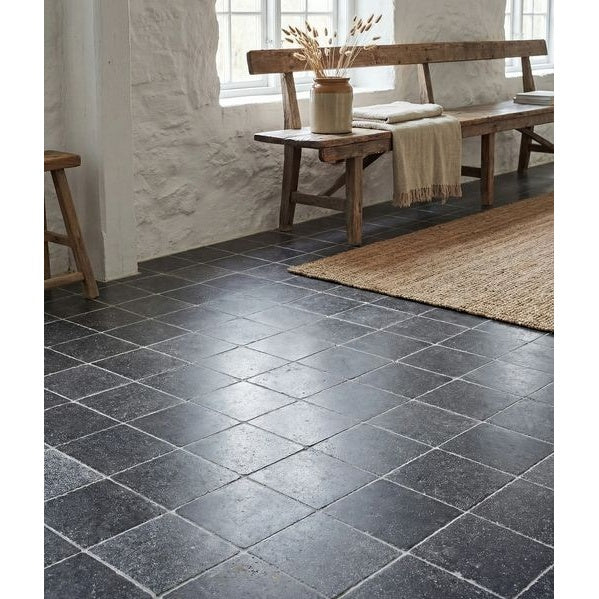 Image of Dark stone tiles on a floor with wooden furniture and a rug.