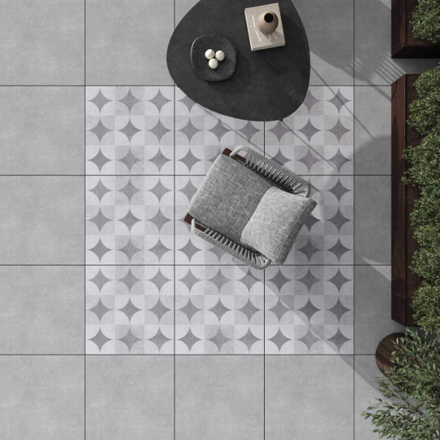 Image of Top-down view of a patterned tile area with a cushioned chair beside a dark, rounded table and surrounding greenery