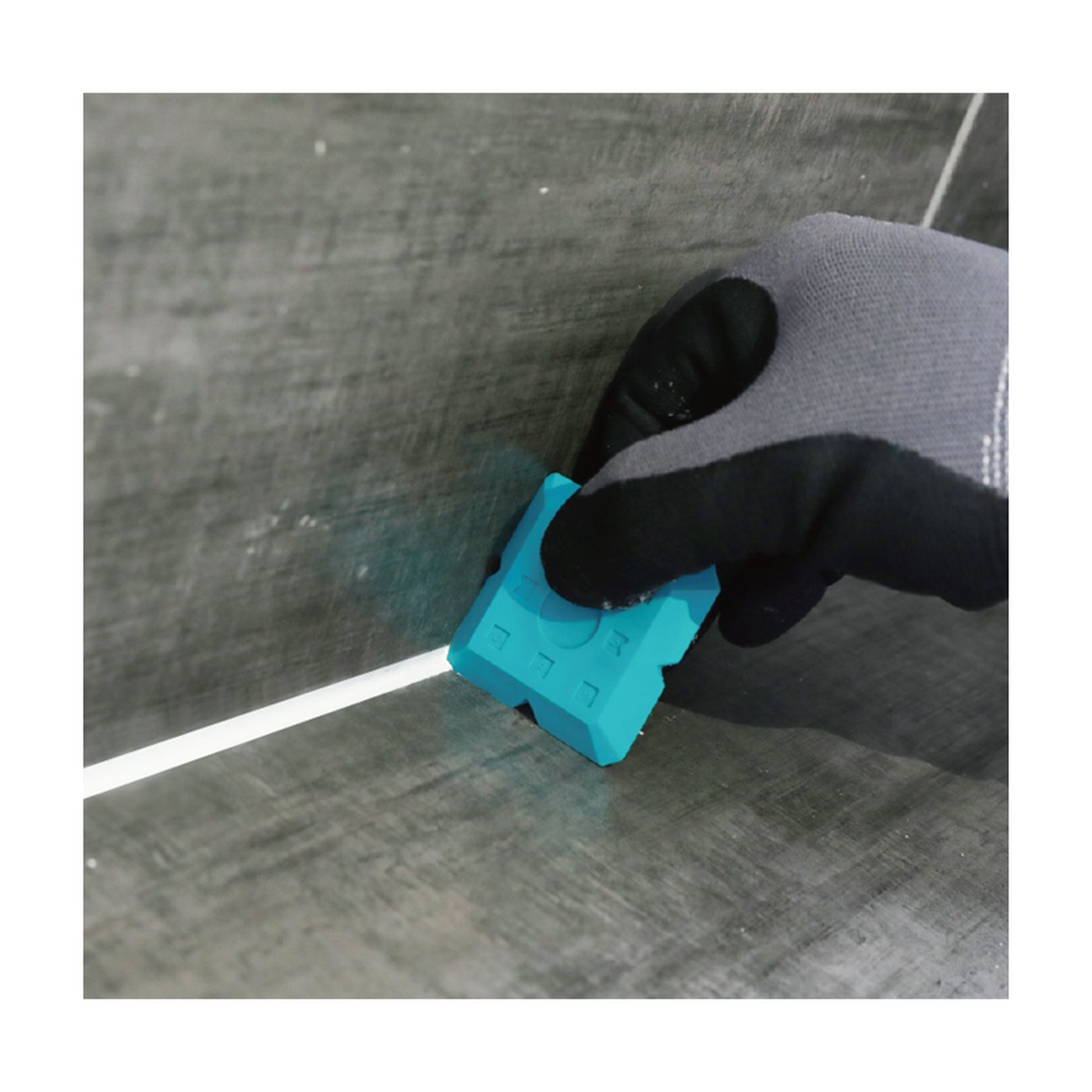 Image of Hand using a blue tile grout scraper on a tiled wall.