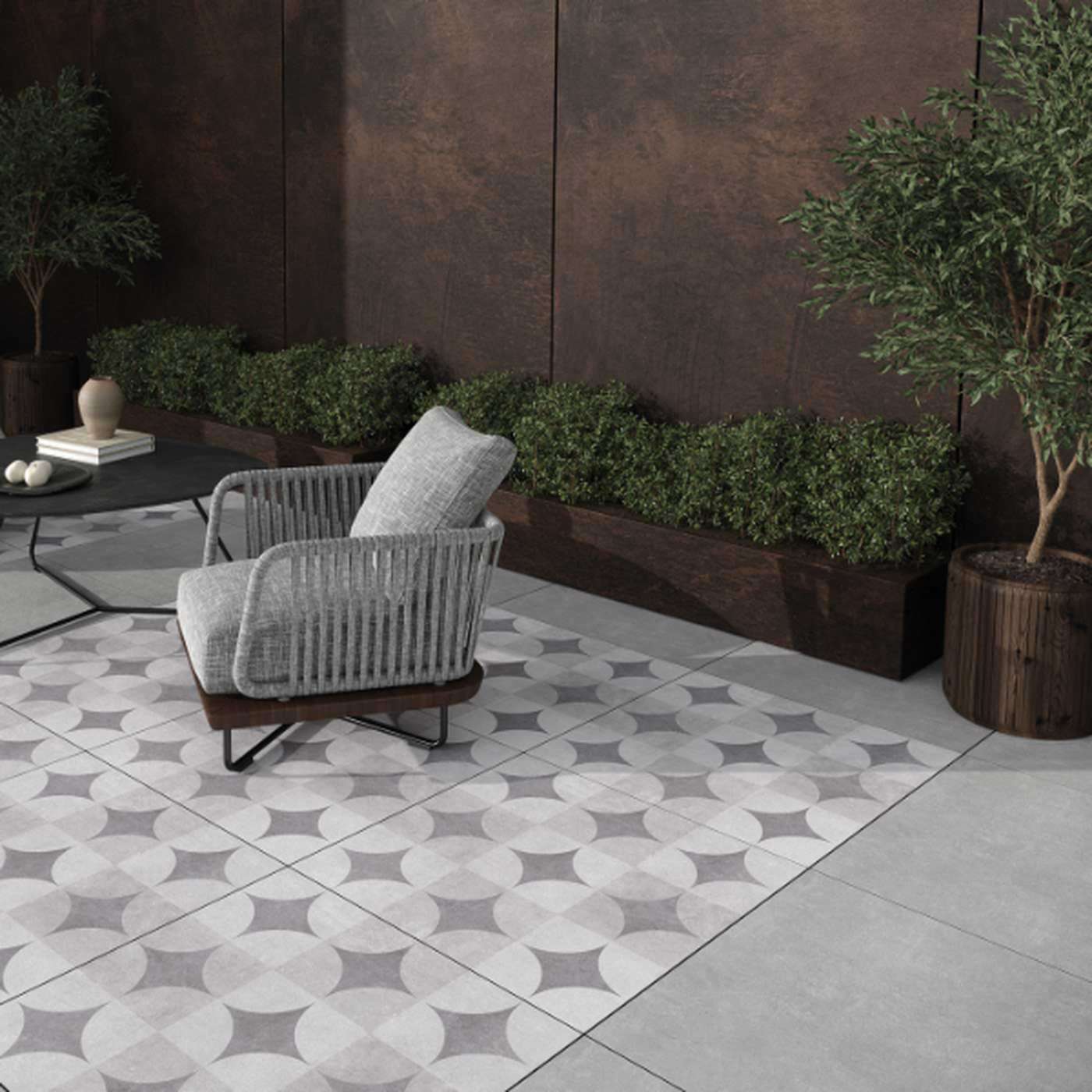 Image of Outdoor seating area with a cushioned woven chair on patterned tiles, surrounded by planters with greenery and a dark textured wall in the background