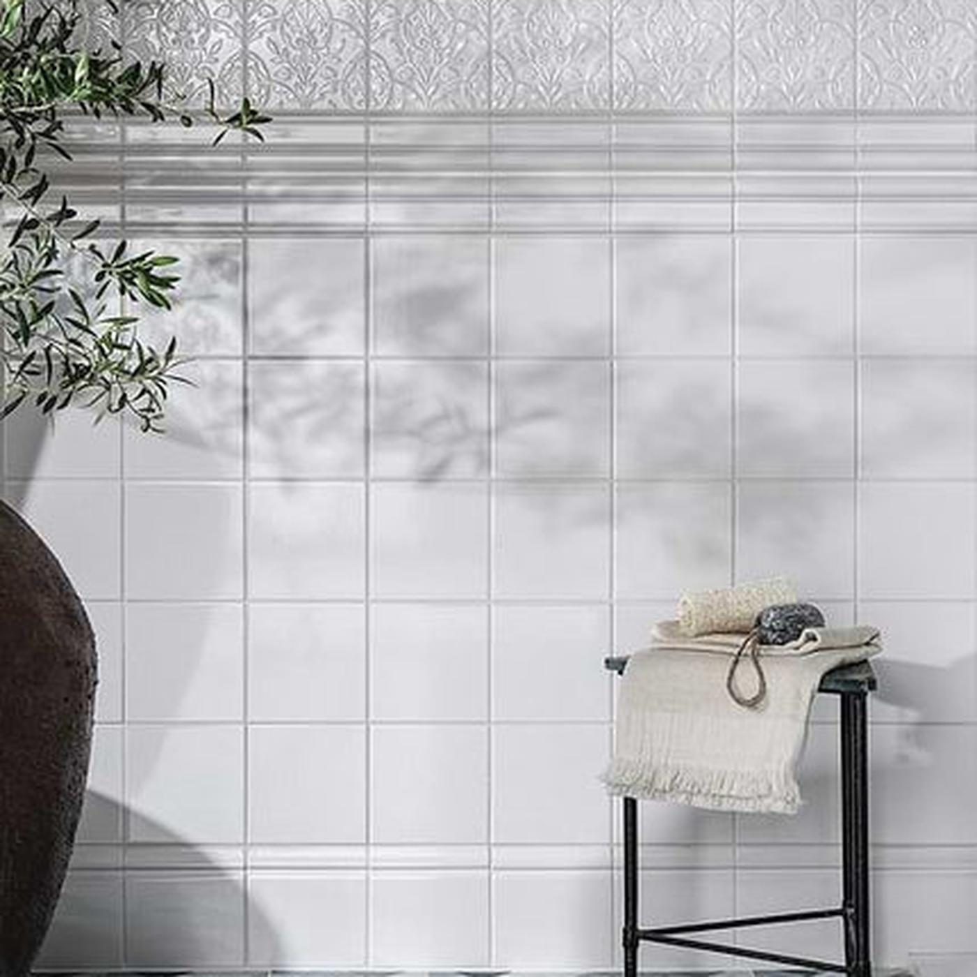 Image of White tiled wall with a plant and stool in the foreground
