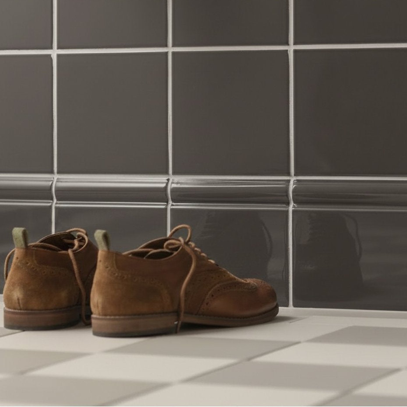 Image of Pair of brown suede shoes on a checkered floor with dark tiled wall.