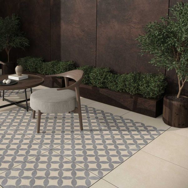 Image of Outdoor seating area featuring a patterned tile section, a round wooden table, a cushioned chair, and surrounding planters with greenery against a dark textured wall