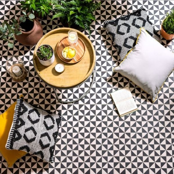 Image of Decorative setting with a wooden tray, candles, and plants on a black and white geometric patterned floor.