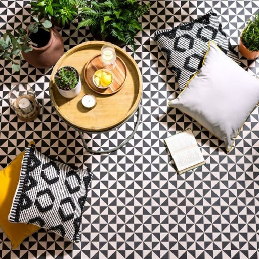Decorative setting with a wooden tray, candles, and plants on a black and white geometric patterned floor.