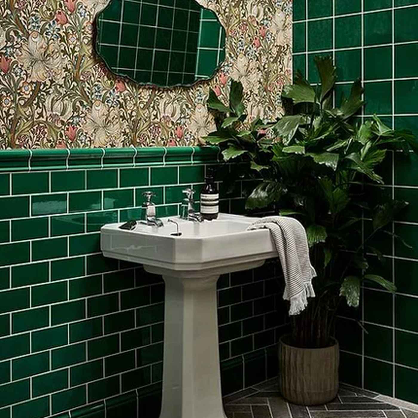 Image of Bathroom with green tiled walls, a white pedestal sink, and decorative mirror.