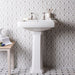 Bathroom with a pedestal sink, patterned grey tile wall, and small wooden side table with decor