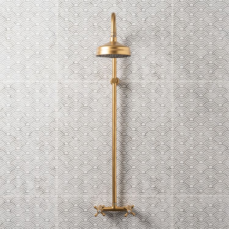 Image of Gold wall‑mounted shower fixture against white tiles with a grey wave pattern.