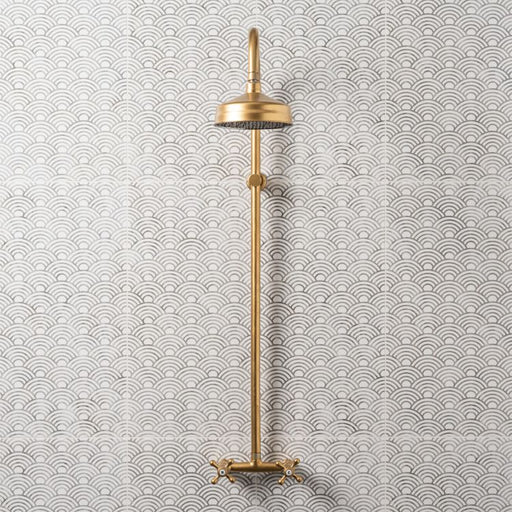 Gold wall‑mounted shower fixture against white tiles with a grey wave pattern.