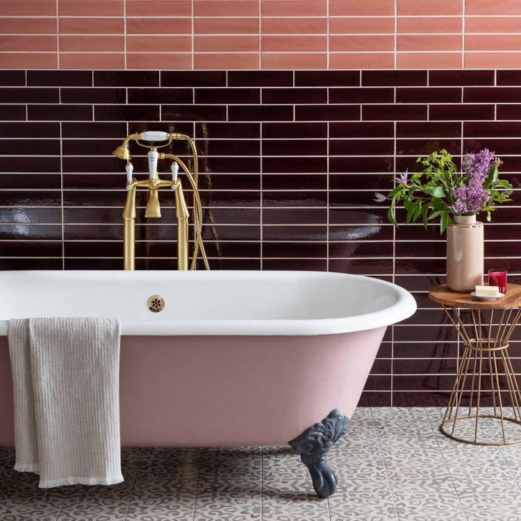 Image of Pink freestanding bathtub in a bathroom with tiled walls and decorative elements.