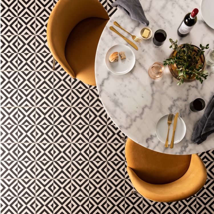 Image of Black-and-white geometric floor tiles beneath a marble dining table set with food, drinks, and mustard‑coloured chairs.