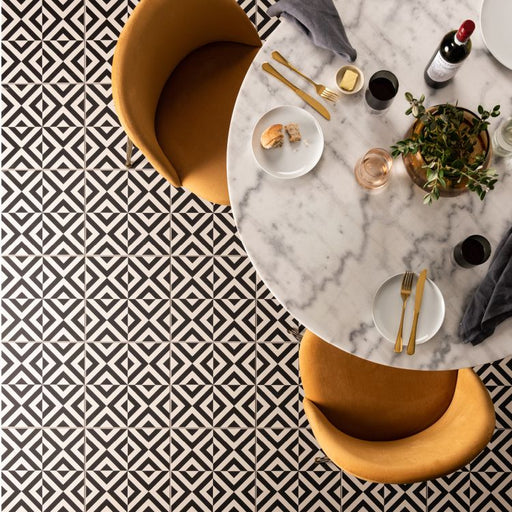 Black-and-white geometric floor tiles beneath a marble dining table set with food, drinks, and mustard‑coloured chairs.