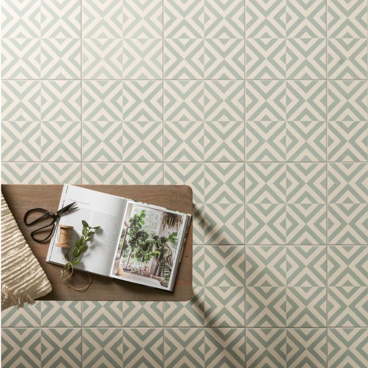 Image of Green and white geometric floor tiles with a small wooden table holding an open plant book, scissors, and a sprig of greenery