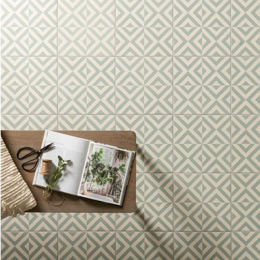 Green and white geometric floor tiles with a small wooden table holding an open plant book, scissors, and a sprig of greenery