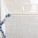 Close-up of a tiled wall with glossy white tiles on top and patterned blue-and-white tiles below, with a white towel featuring blue tassels hanging on the left.