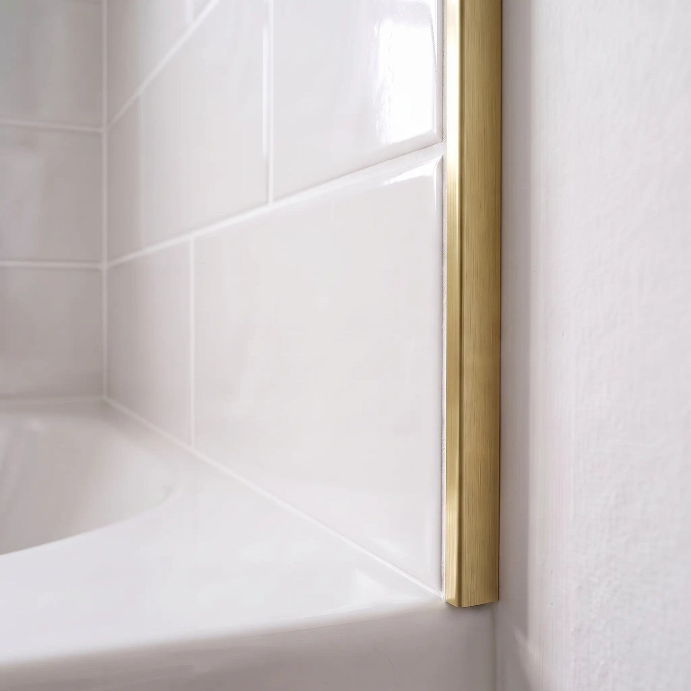 Image of Close-up of a polished brass straight edge tile trim finishing the edge of glossy white ceramic wall tiles above a bath