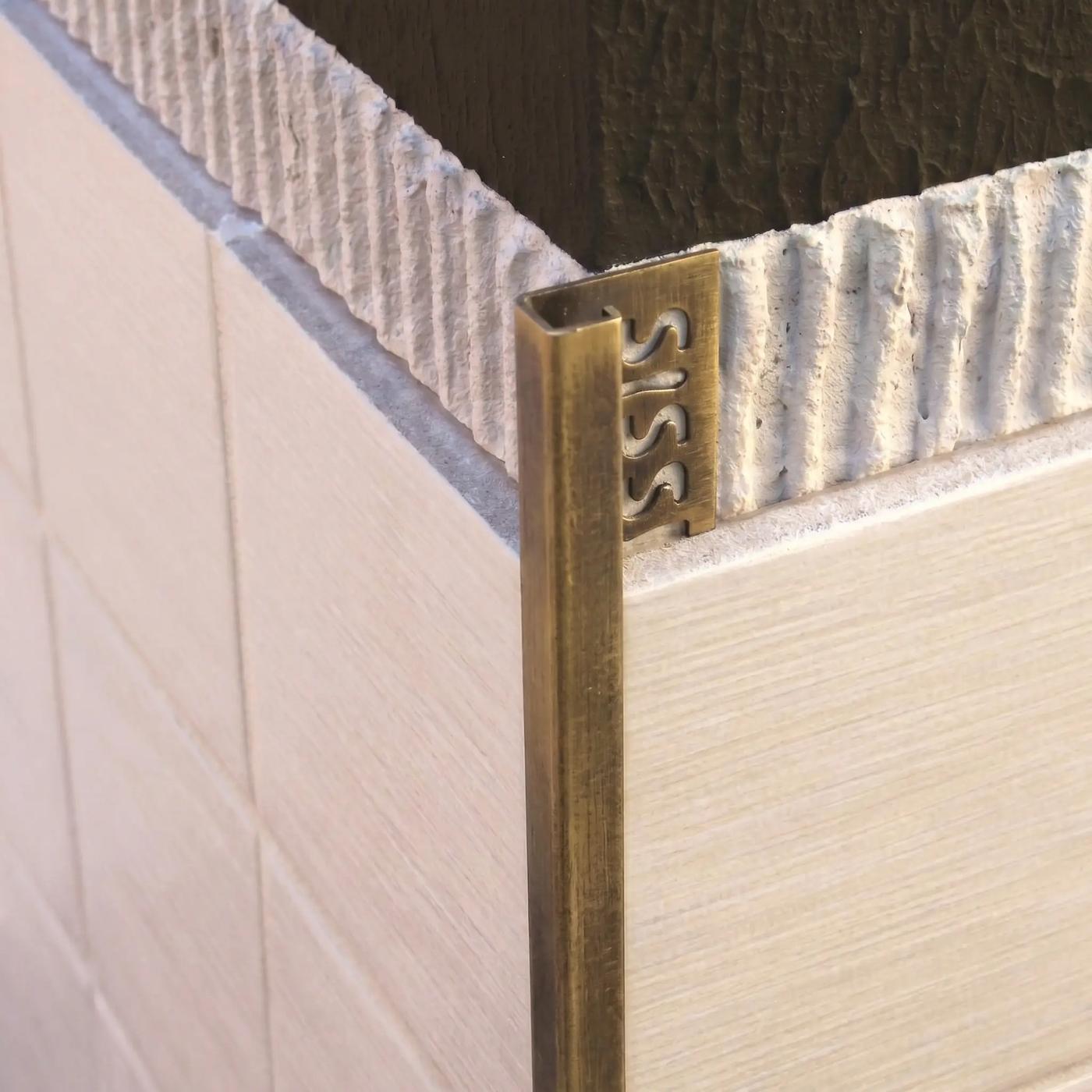 Image of Close-up of an antique brass square edge tile trim fitted to an external corner of cream ceramic wall tiles.