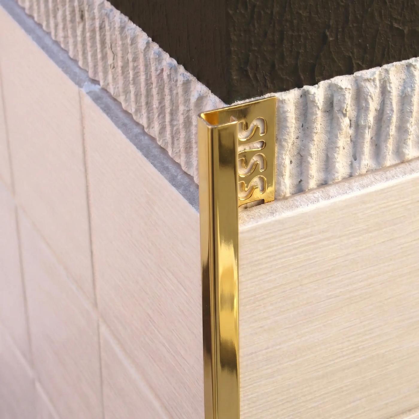 Image of Close-up of a bright gold square edge tile trim fitted to an external corner of cream ceramic wall tiles