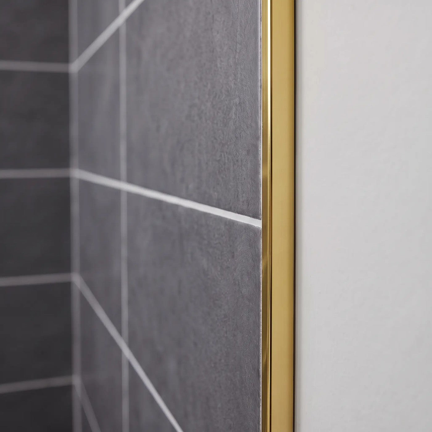 Image of Close-up of a bright gold tile trim fitted to the edge of dark grey wall tiles in a bathroom.