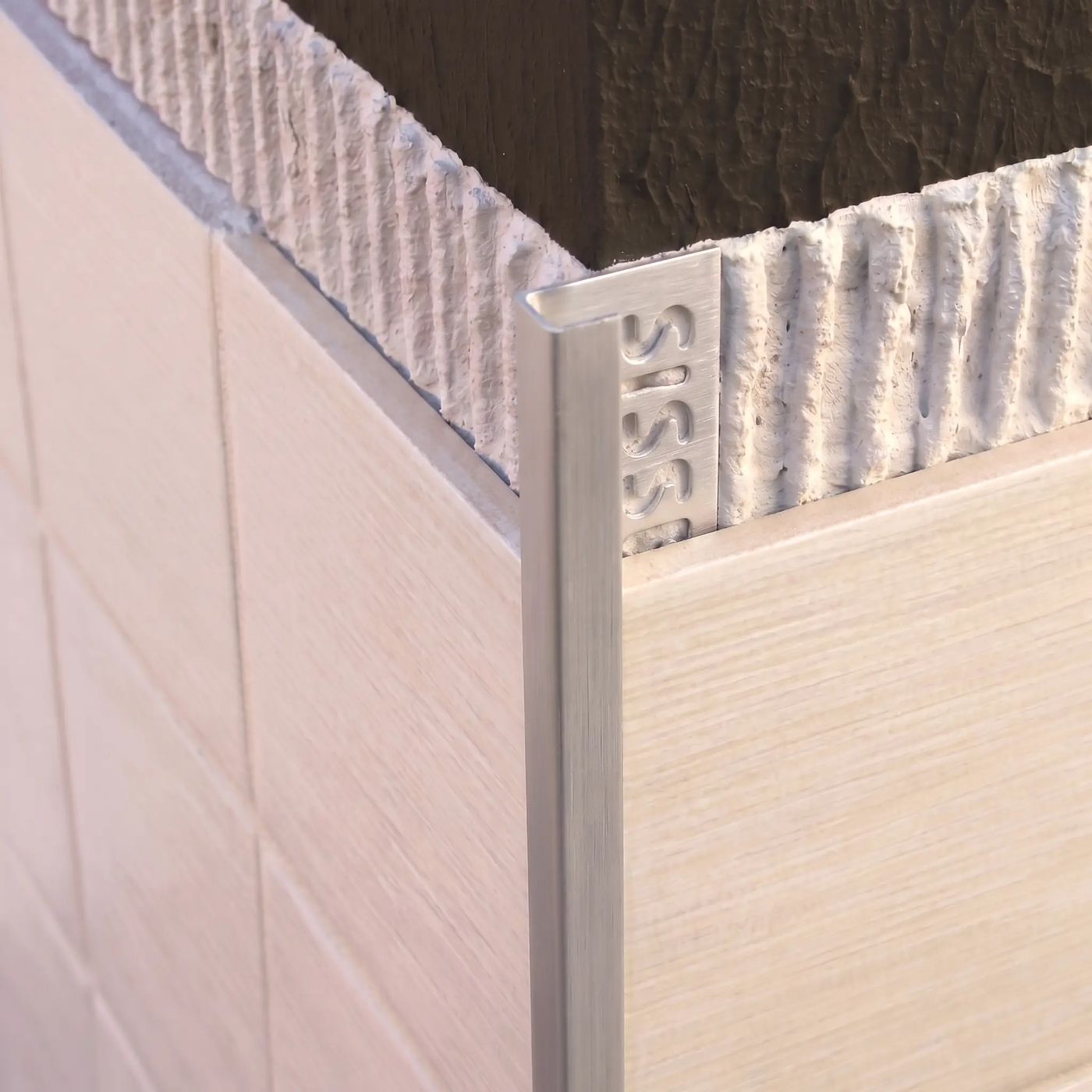 Image of Close-up of a brushed silver square edge tile trim fitted to an external corner of cream ceramic wall tiles.