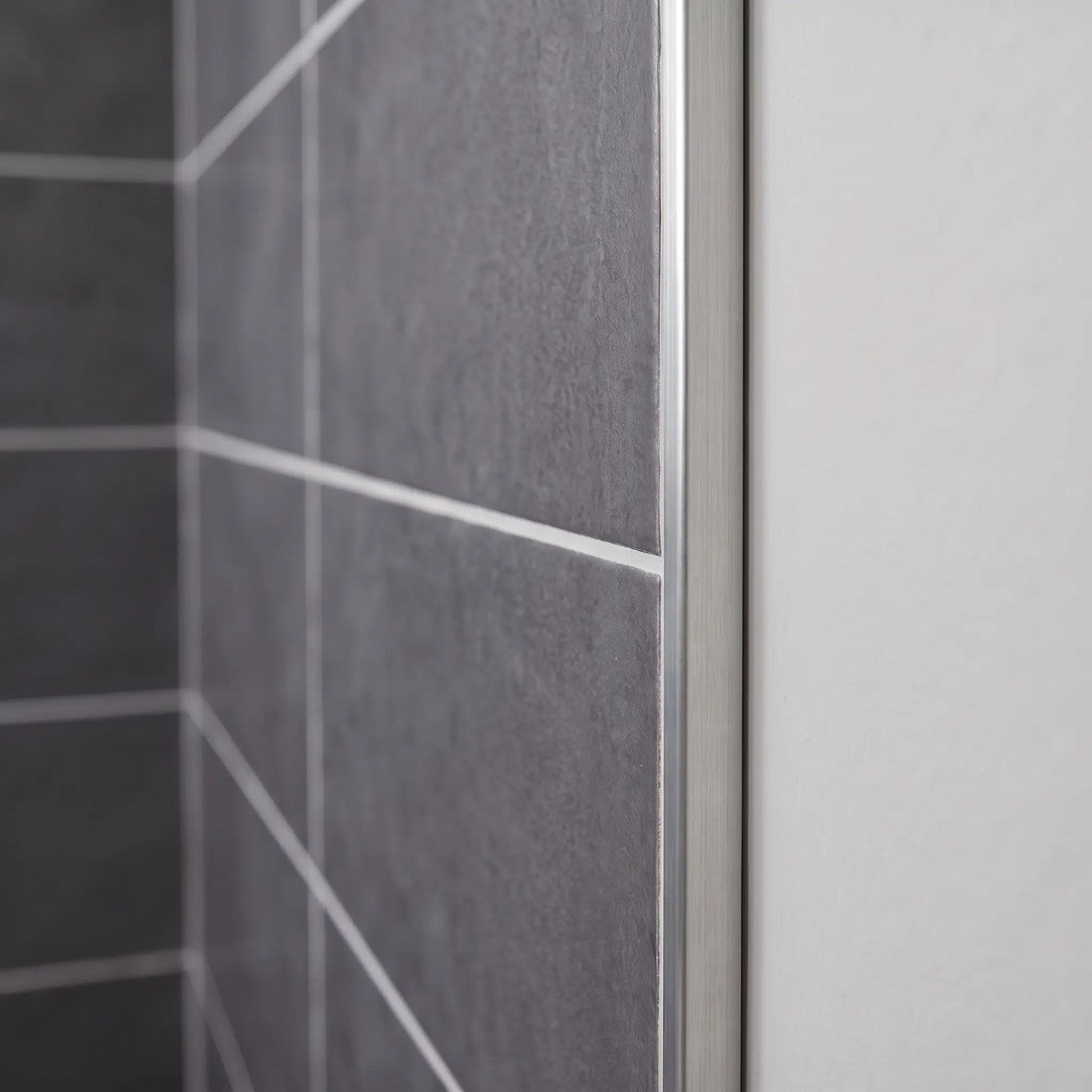 Image of Close-up of a brushed silver tile trim fitted to the edge of dark grey wall tiles in a bathroom.