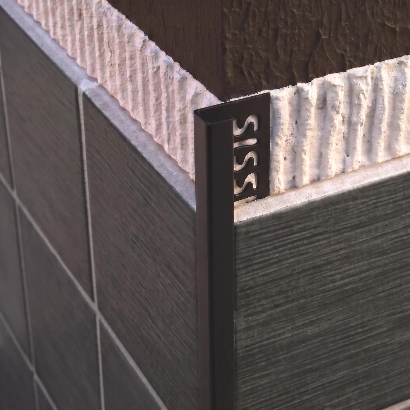Image of Close-up of a matt black square edge tile trim fitted to an external corner of dark grey ceramic wall tiles.