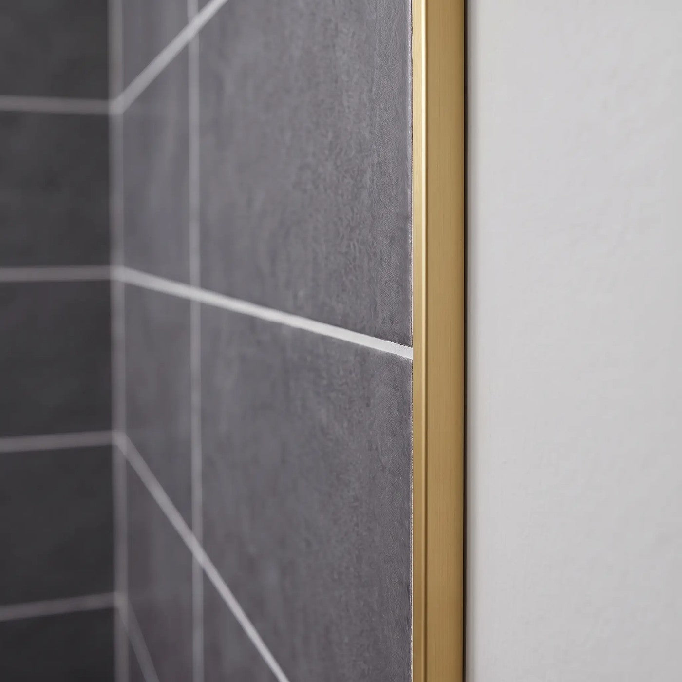 Image of Close-up of a matt gold tile trim fitted to the edge of dark grey wall tiles in a bathroom