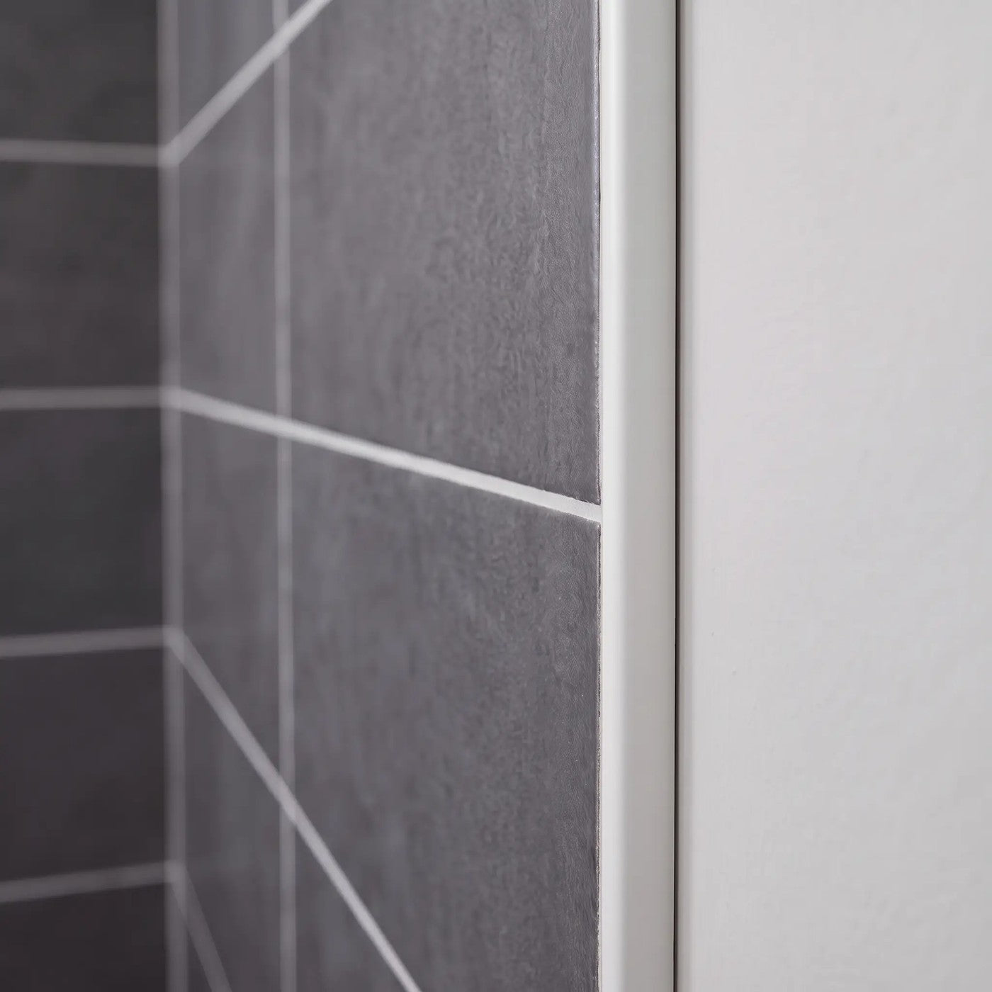 Image of Close-up of a matt white tile trim fitted to the edge of dark grey wall tiles in a bathroom.