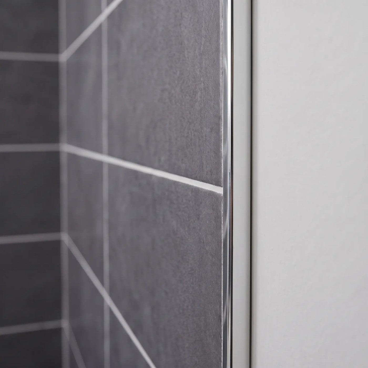 Image of Close-up of a polished silver tile trim fitted to the edge of dark grey wall tiles in a bathroom.
